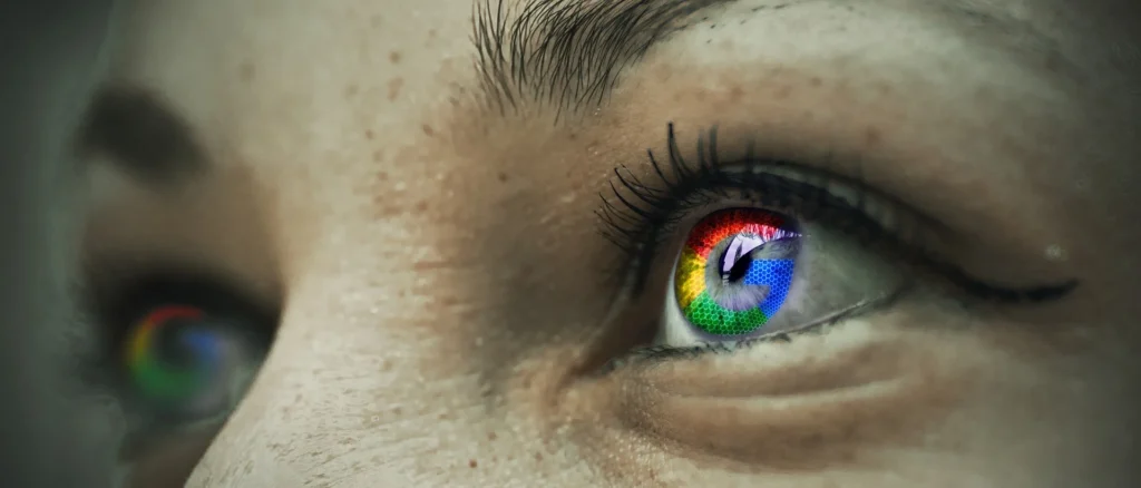 A detailed macro shot of a person's eye, where the iris has been replaced with the colorful Google "G" logo. The second eye, also with the logo, is visible but blurred in the background.